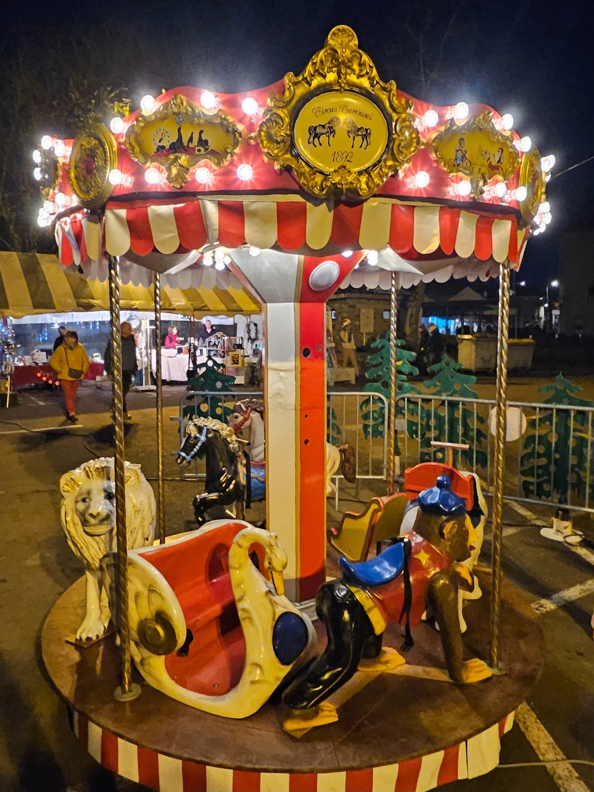 Carrousel rouge et crème illuminé, installé en extérieur.